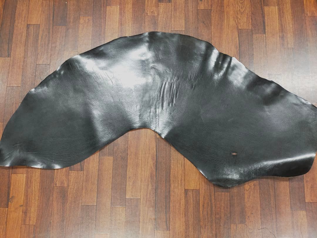 A large black horse leather hide laid out flat on a wooden floor.