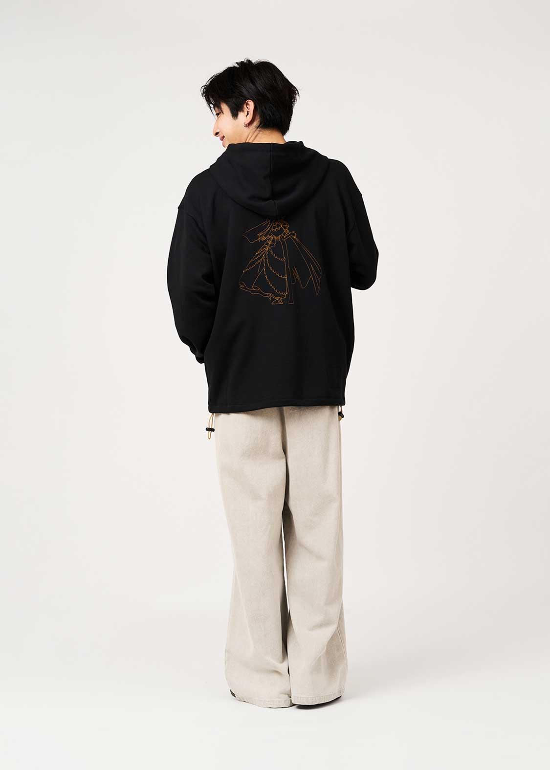 A model seen from behind wearing the black zip parka with a gold line-art back print.