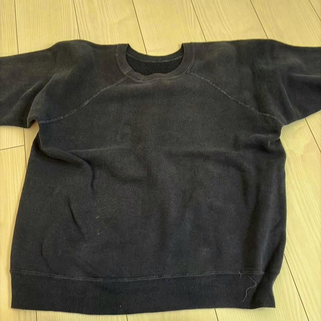 A black-navy raglan-sleeve cotton sweatshirt laid flat on a wooden floor.