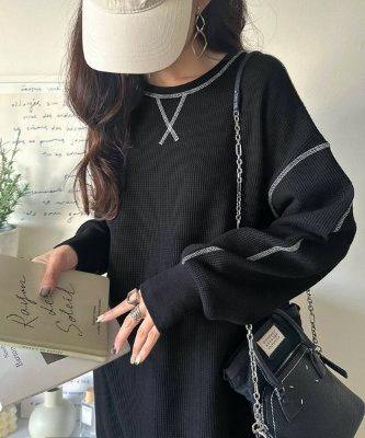 Model wearing a black long-sleeve women's dress with visible light contrast stitching and a small black shoulder bag.