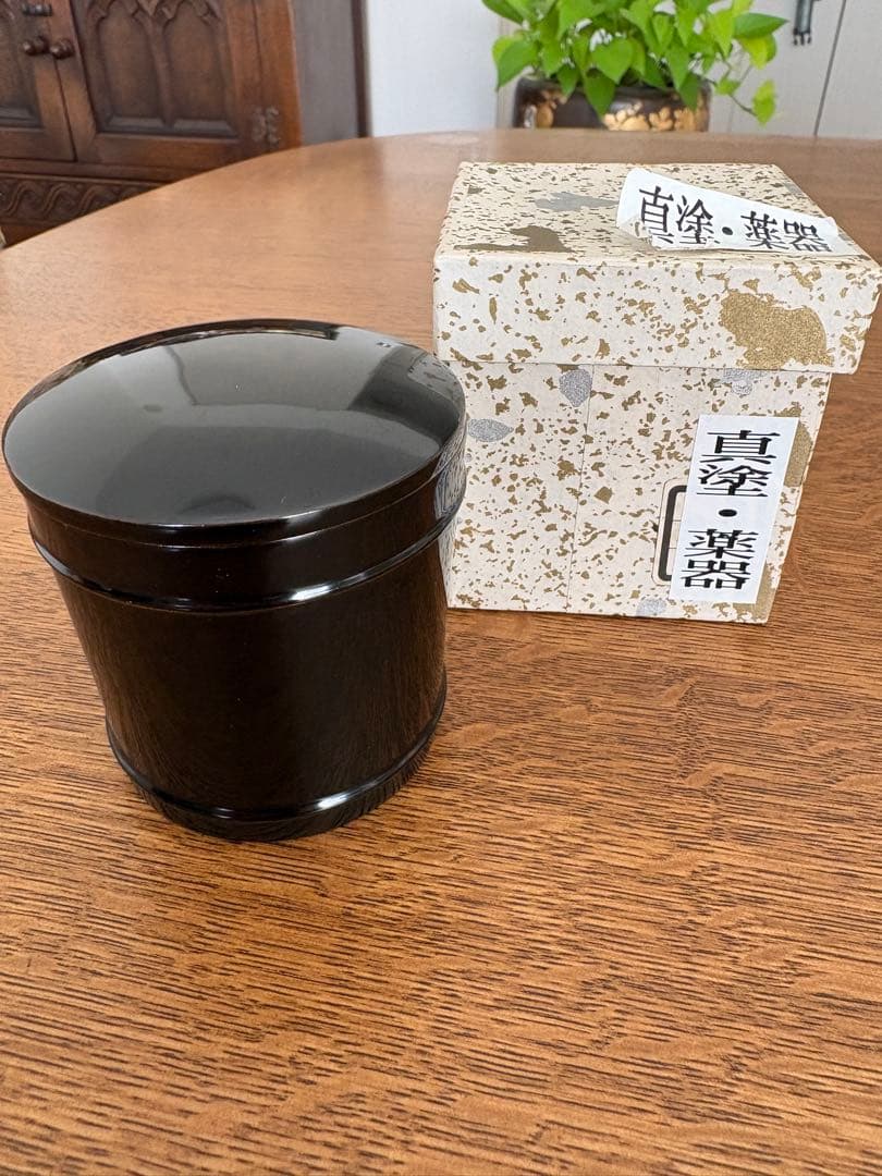 Black lacquered natsume (tea caddy) with its box on a wooden table.