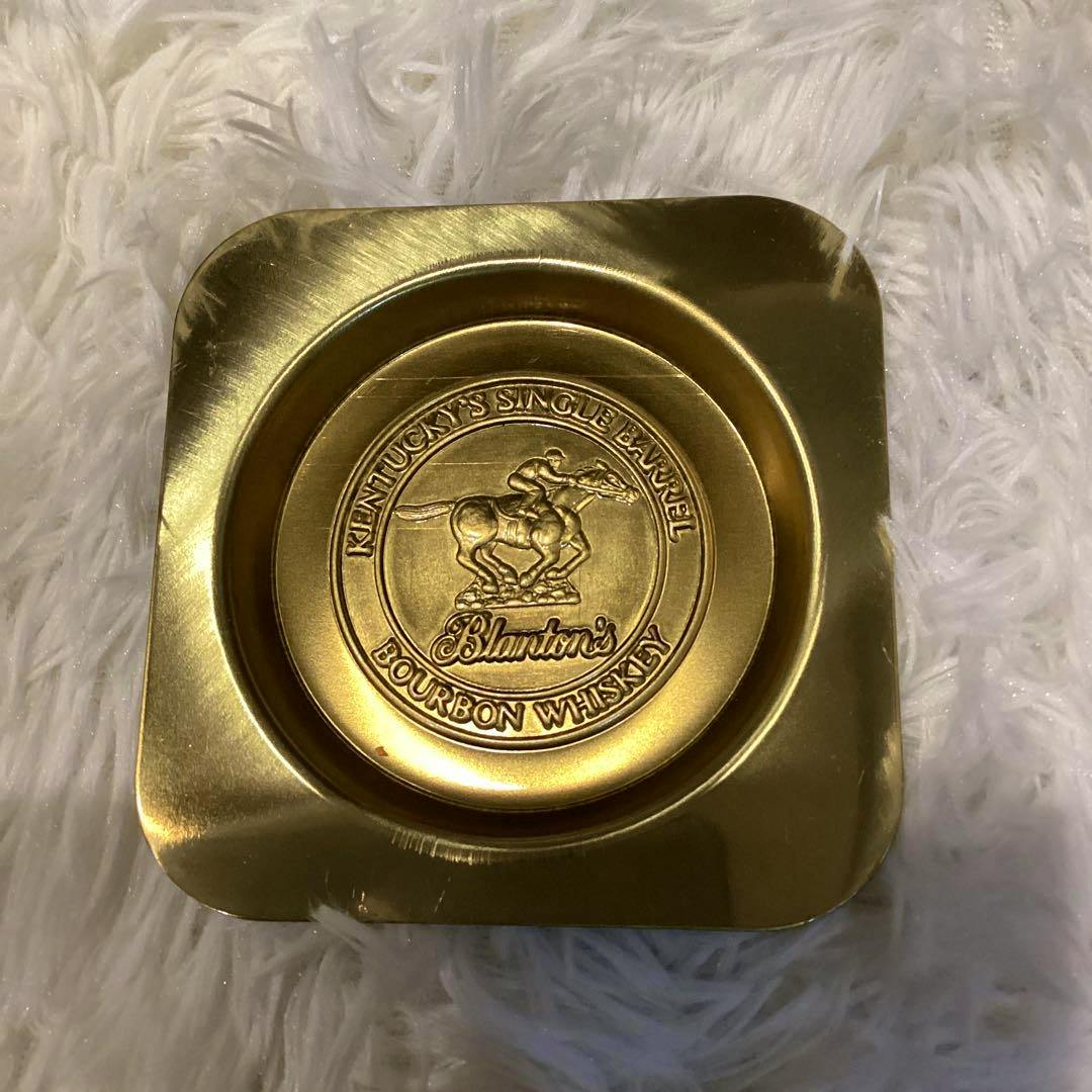 Gold stainless-steel Blanton's tray showing an embossed horse-and-rider logo on a white fluffy background.
