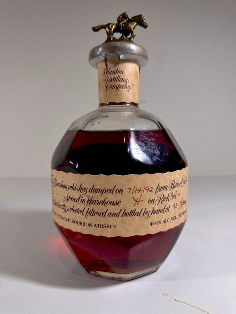 Faceted glass whiskey bottle with a horse-shaped stopper and a torn paper label with handwritten notes.