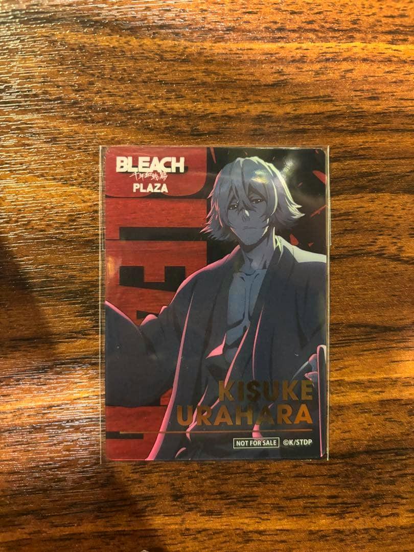 Photo of a BLEACH PLAZA foil clear card featuring Kisuke Urahara in a protective sleeve on a wooden surface.