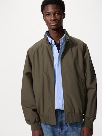 Male model wearing an olive-green zip-up jacket over a light blue button-down shirt and jeans.