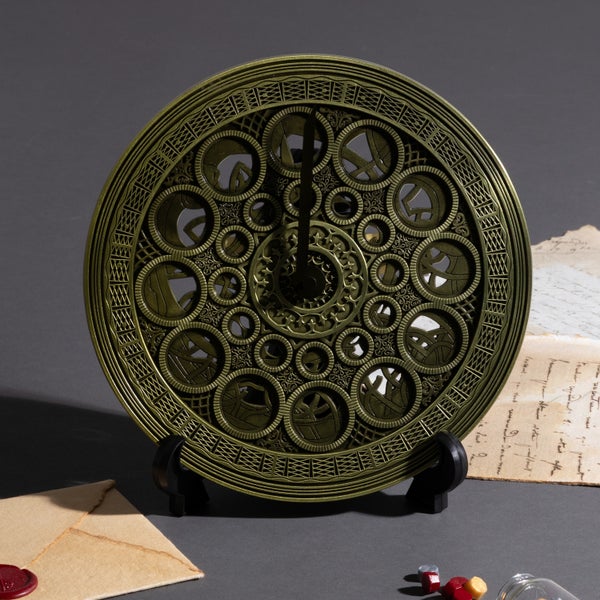 Circular Clocktower model desk alarm clock with ornate gear-like cutouts and clock hands displayed on a small black stand.
