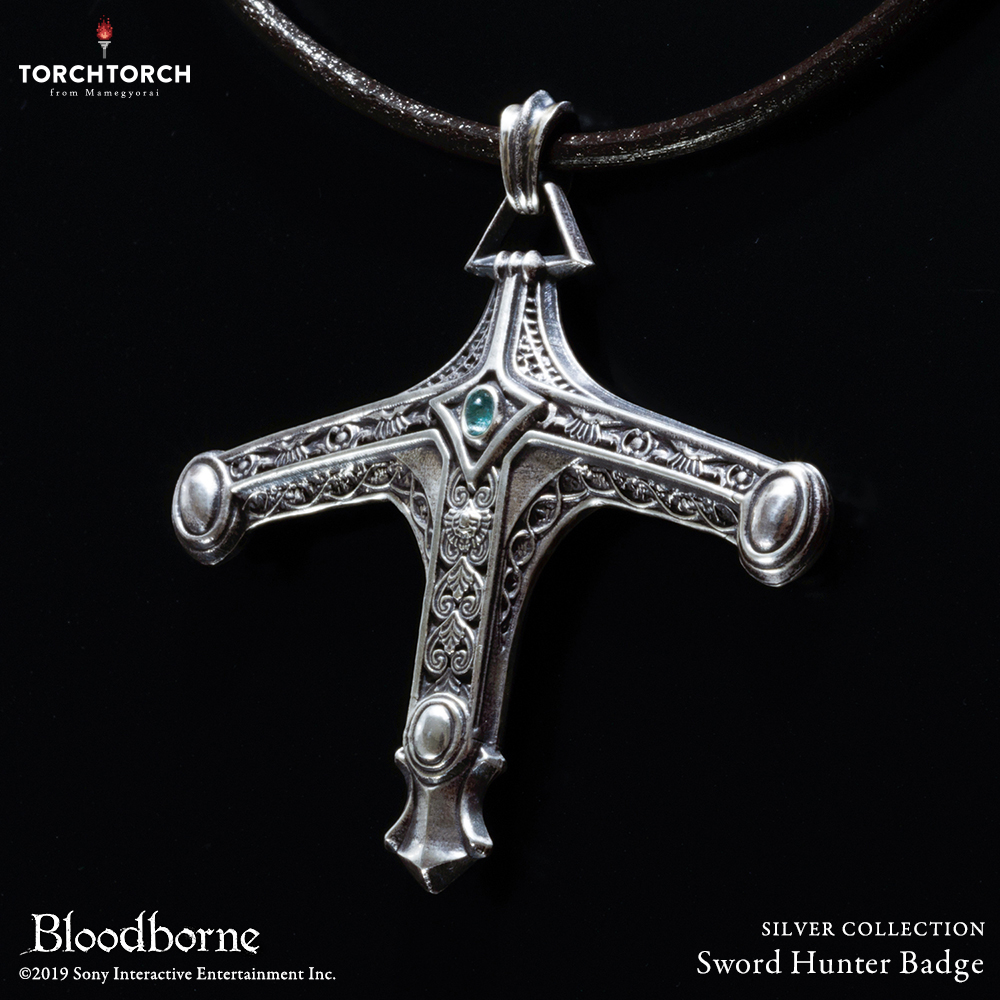 Close-up photo of the Bloodborne × TORCH TORCH silver "Sword Hunter Badge" pendant on a cord against a black background.