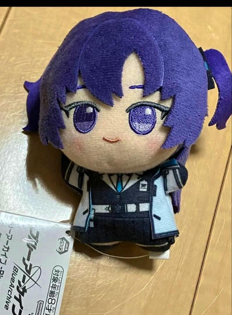 Front view of the ブルーアーカイブ ちびぐるみ 早瀬ユウカ plush resting on a wooden surface with its tag visible.