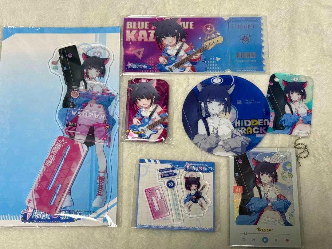 Photo of the Blue Archive China 3rd Anniversary Kazusa goods set laid out, showing acrylic stands, keychains, badges, and other character merchandise featuring Kazusa.