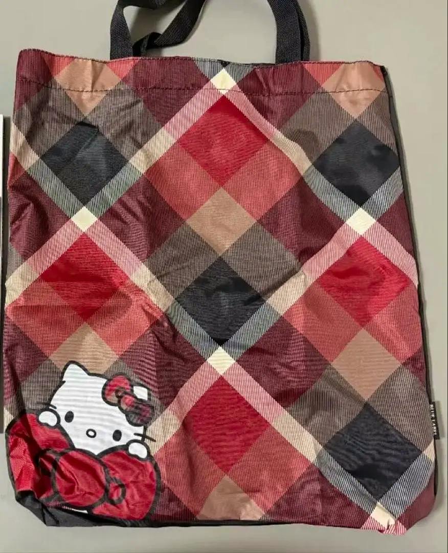 Red and brown checkered nylon tote bag with black handles and a Hello Kitty graphic peeking from the lower-left corner.