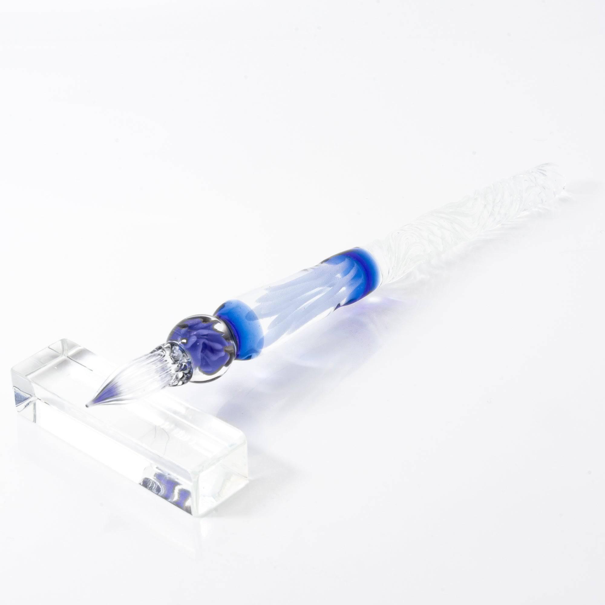 Blue-accented glass dip pen resting on a clear pen rest on a white background.