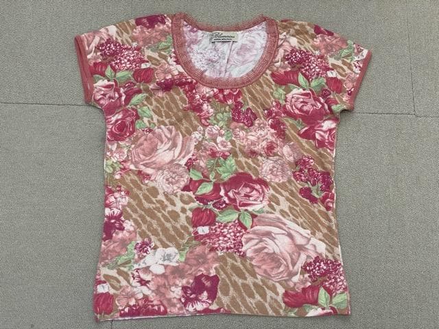 Pink floral-motif cotton knit women's short-sleeve shirt laid flat on a gray surface.