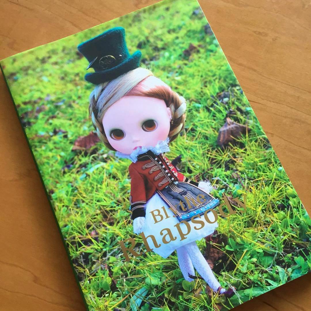 Front cover of the book showing a Blythe-style doll standing on grass with the title ブライスラプソディ visible.