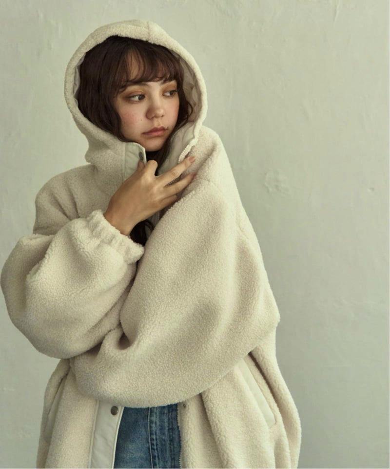 Woman wearing a light beige boa hooded women's jacket with plush texture and the hood up.