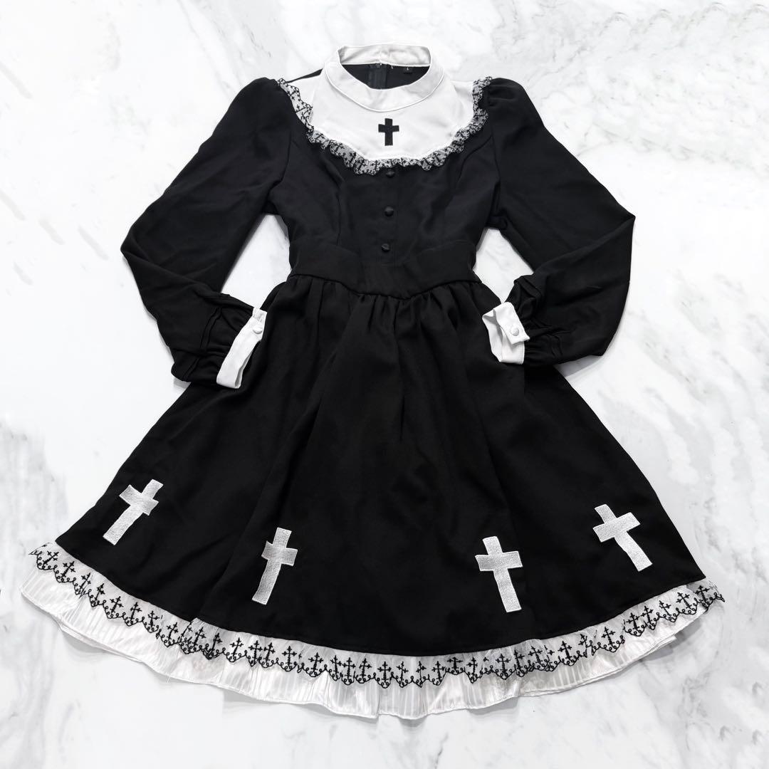Black and white gothic lolita women's dress with cross appliqués and frilled hem laid flat on a marble background.