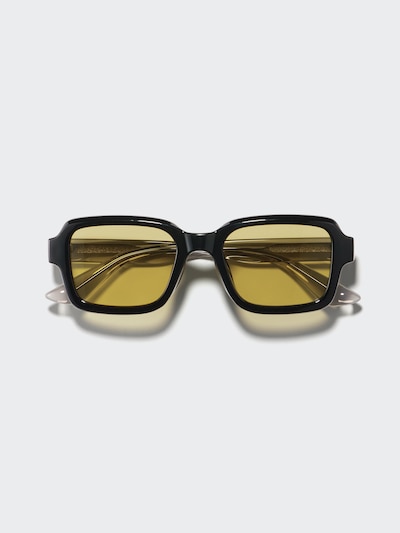 Front view of square black sunglasses with yellow lenses on a light background.
