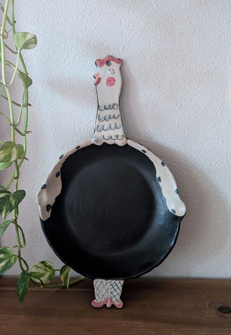 A front view of the griddle pan with a black cooking surface and a decorative chicken-shaped handle.