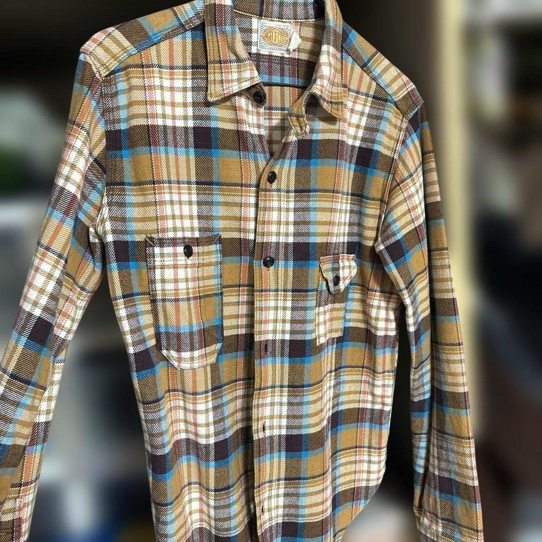A men's brown, blue, and white plaid long-sleeve shirt hanging on a hanger showing the front with two chest pockets.