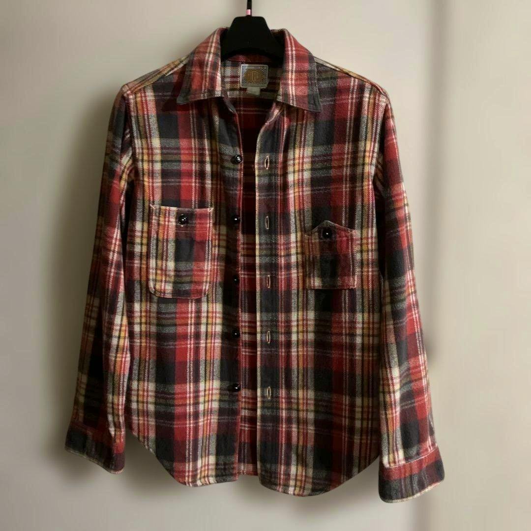 Front view of a red, black, and cream plaid flannel shirt hanging on a hanger showing chest pockets and button closure.
