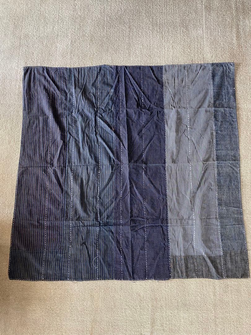 Rectangular indigo patchwork cotton hand towel with vertical striped panels and visible hand-stitching laid flat on a beige surface.