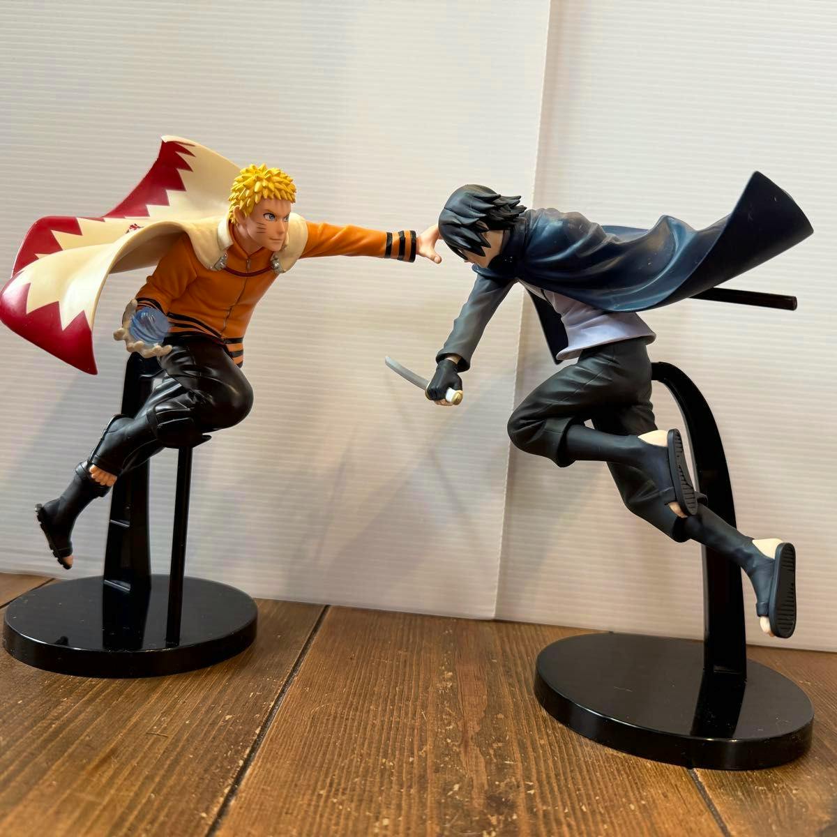 Two plastic VIBRATION STARS figures (Naruto wearing a Hokage cloak and Sasuke) mounted on black display stands posed facing each other.