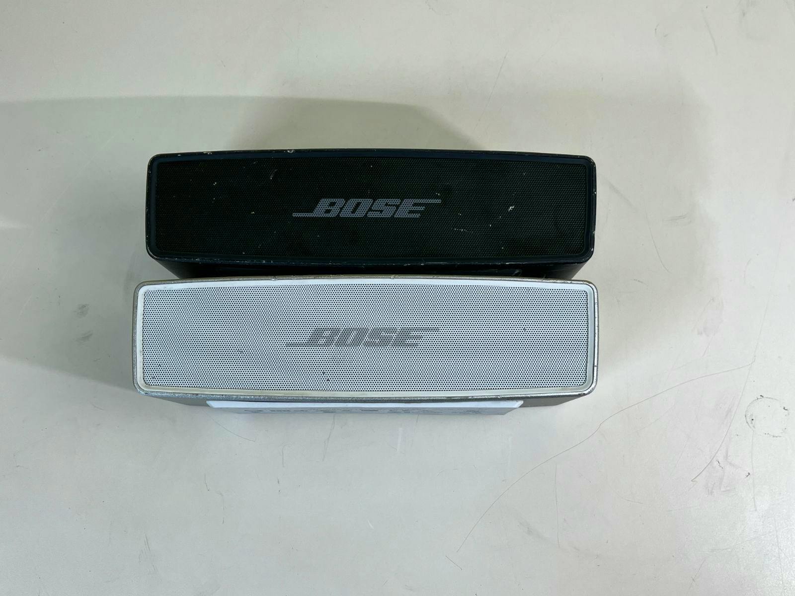 Two BOSE SoundLink Mini II Bluetooth speakers, one black and one silver, shown from the front on a light surface.