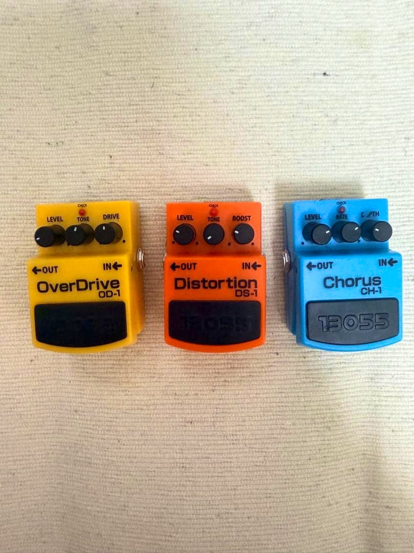 Three miniature BOSS effect pedal figures (OverDrive OD-1, Distortion DS-1, Chorus CH-1) placed side by side on fabric.