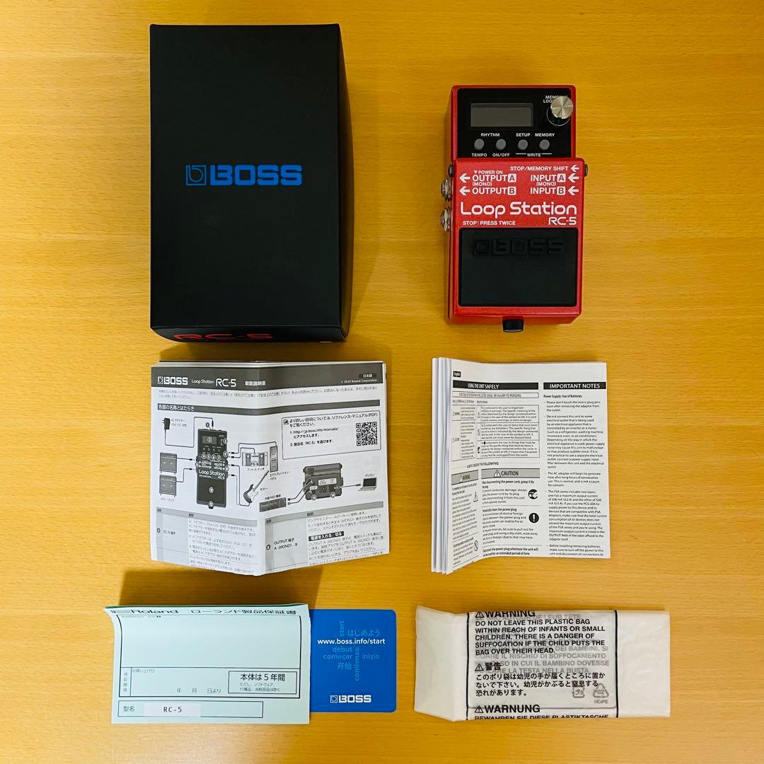 Top-down photo of a red BOSS RC-5 Loop Station pedal with its black BOSS box, manuals, and paperwork on a wooden surface.