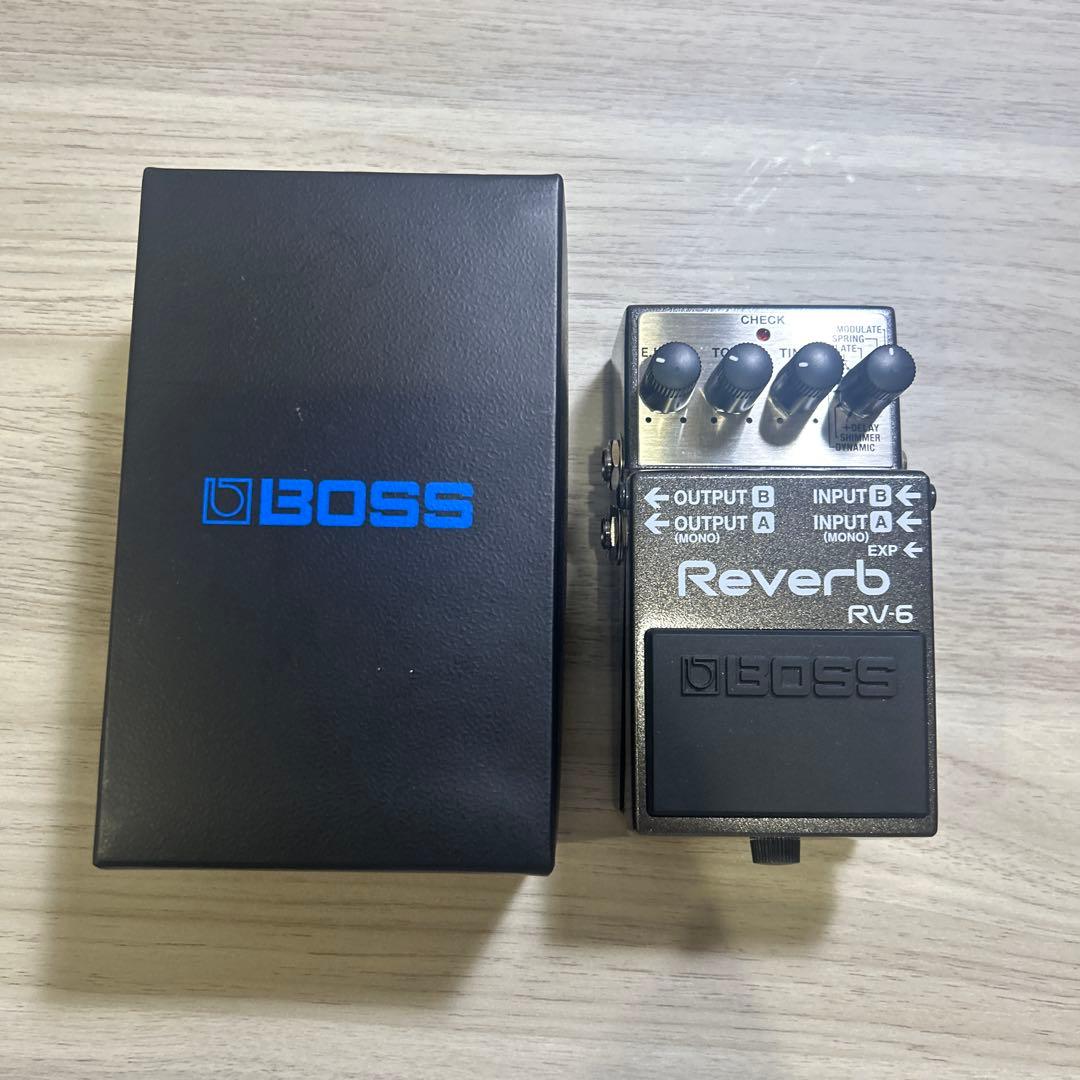 Top-down photo of a BOSS Reverb RV-6 guitar effector pedal next to its black BOSS box on a light wood surface.
