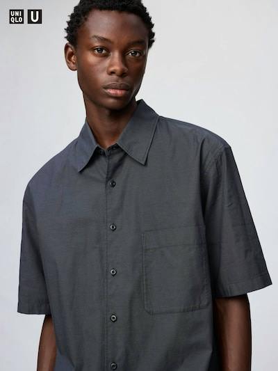 Close-up of a male model wearing a dark gray short-sleeve boxy button-up cotton shirt with a chest pocket.