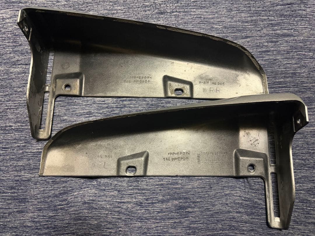 Two black plastic bumper splash guards (front/rear set) laid on a fabric surface, showing their inner faces.