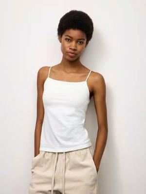 Model wearing a white narrow‑strap camisole tank top shown from the front.