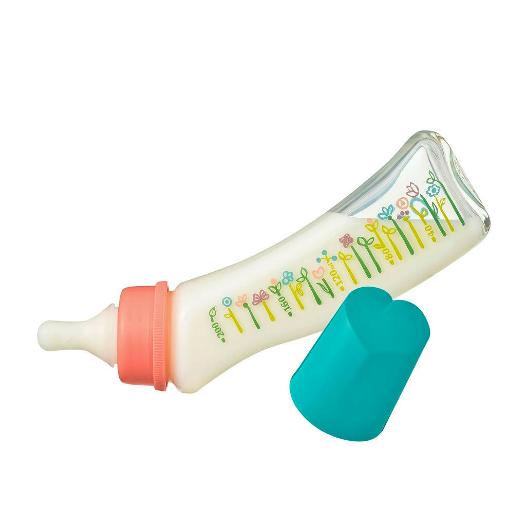 Glass baby bottle with flower measurement markings, a nipple attached, and a detached turquoise cap.