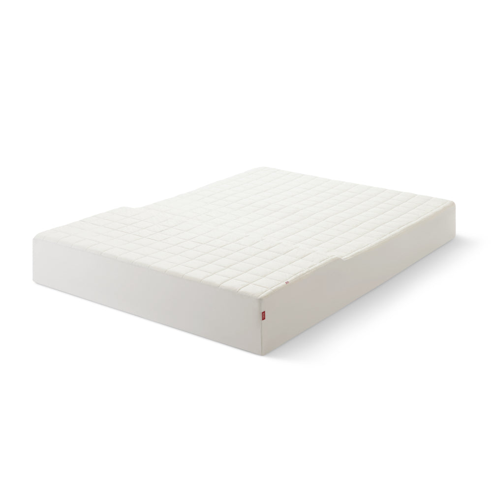 Angled photo of a white quilted mattress protector covering a mattress.