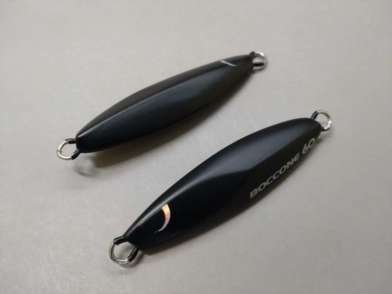 Two solid black BREED Boccone 150g fishing lures lying on a light gray surface.