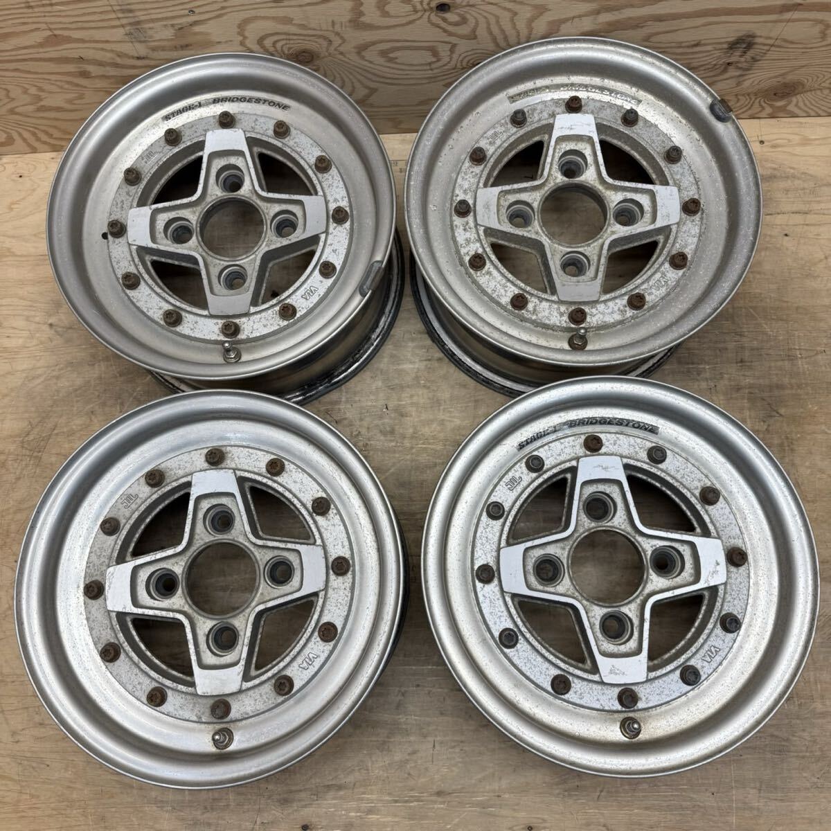 Four Bridgestone ZONA Stage 1 13-inch car wheels (4-hole) laid flat on a wooden surface showing their front faces and bolt holes.