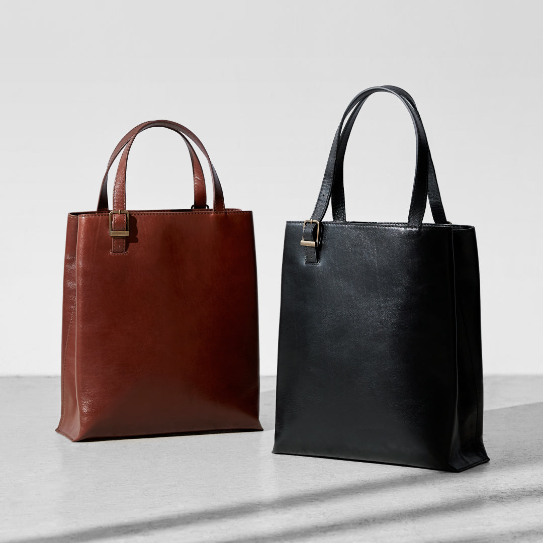 Two Bright V Tote bags in brown and black cow leather displayed upright against a light background.