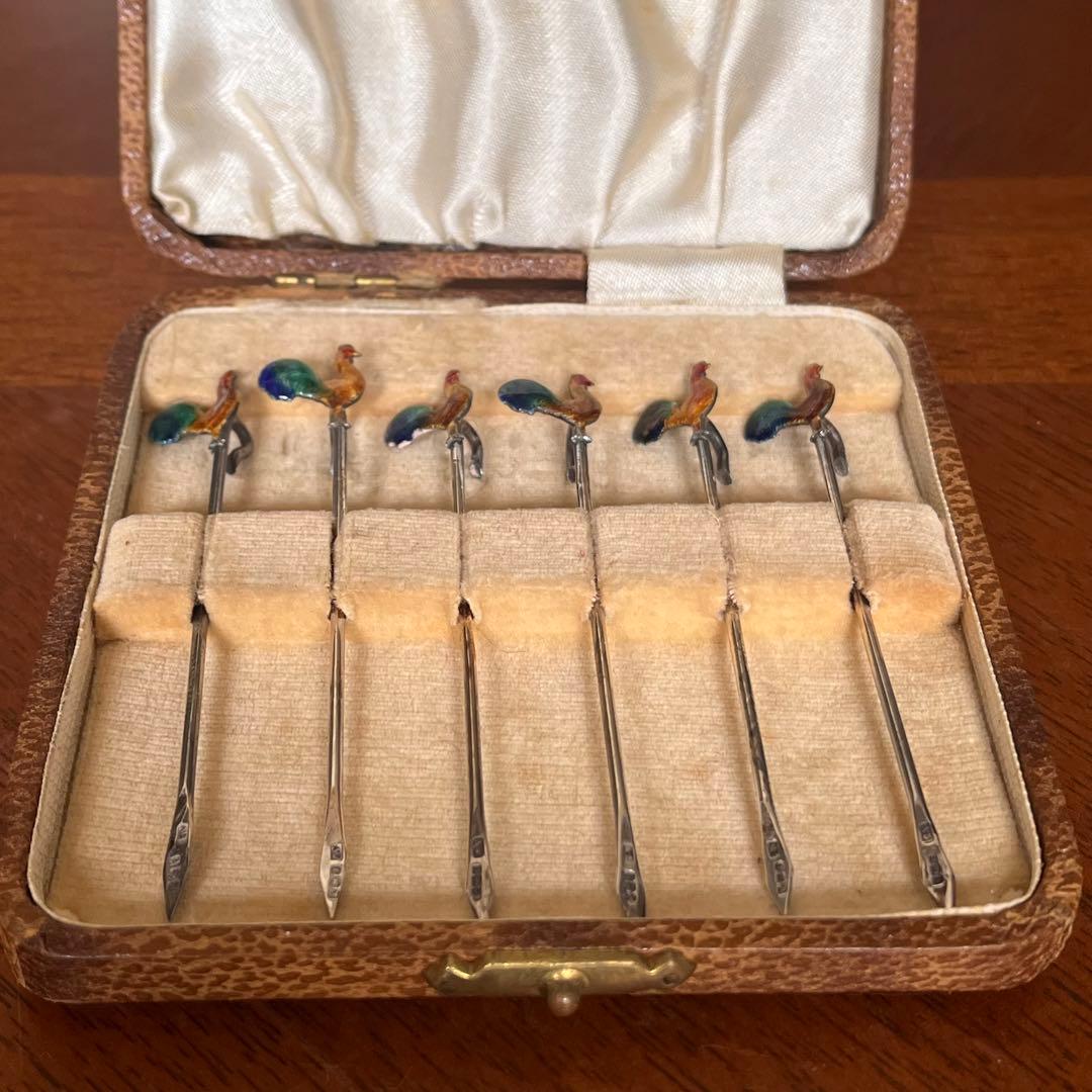 Six stainless-steel drink picks with cloisonné rooster tops displayed in a velvet-lined presentation box.