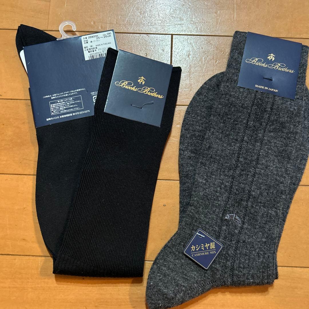 Two Brooks Brothers high socks (black and gray) with labels attached laid flat on a wooden floor.