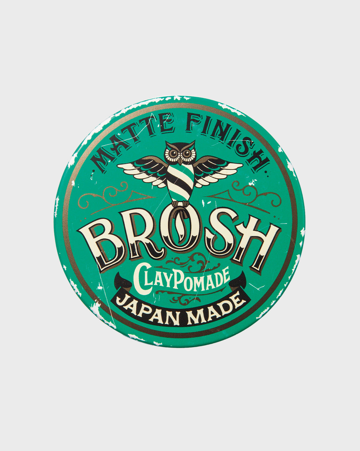 Top-down photo of the BROSH Clay Pomade tin lid showing the green matte-finish label with an owl logo and the word “BROSH.”