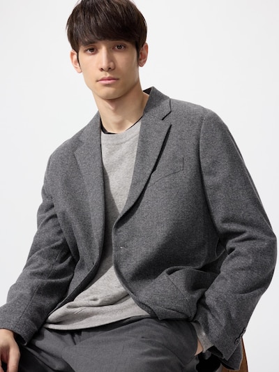Male model seated wearing a grey herringbone brushed-jersey men's jacket over a light grey sweater against a white background.