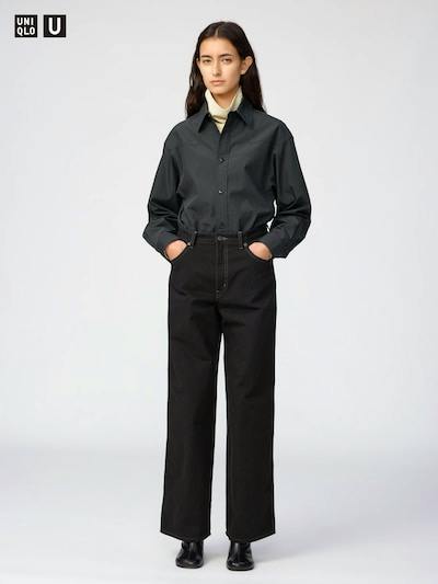 Front view of a female model wearing the women's black wide-length pants from the listing, hands in pockets, paired with a dark button-up shirt and black shoes.