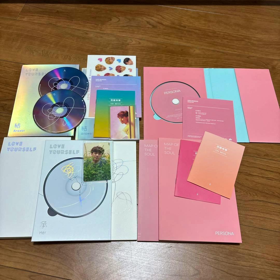 Several BTS albums, CDs, booklets, and photocards laid out on a wooden floor.