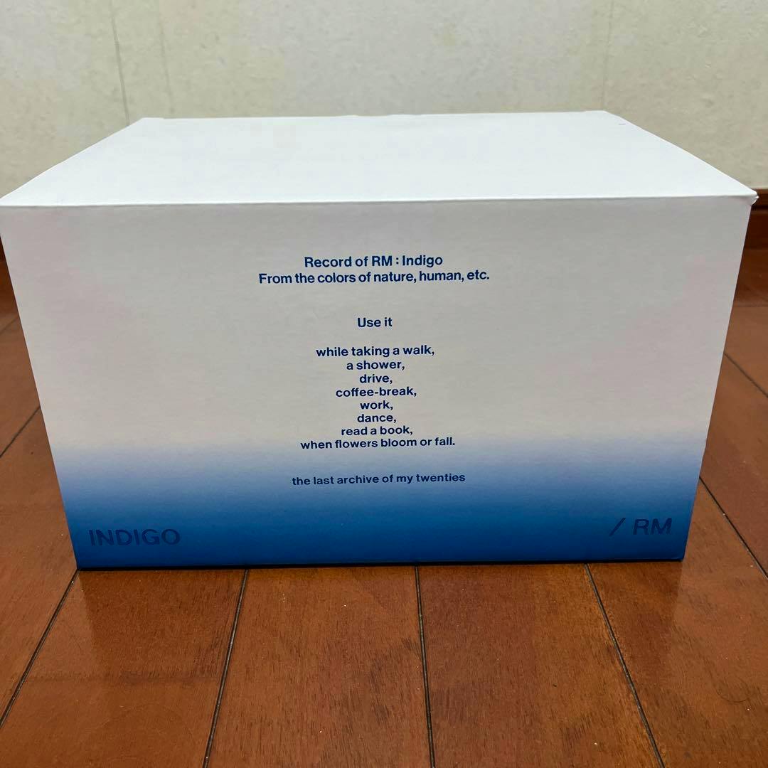 Front view of the BTS MARCH BOX #16 white box with a blue gradient and printed text visible on a wooden floor.
