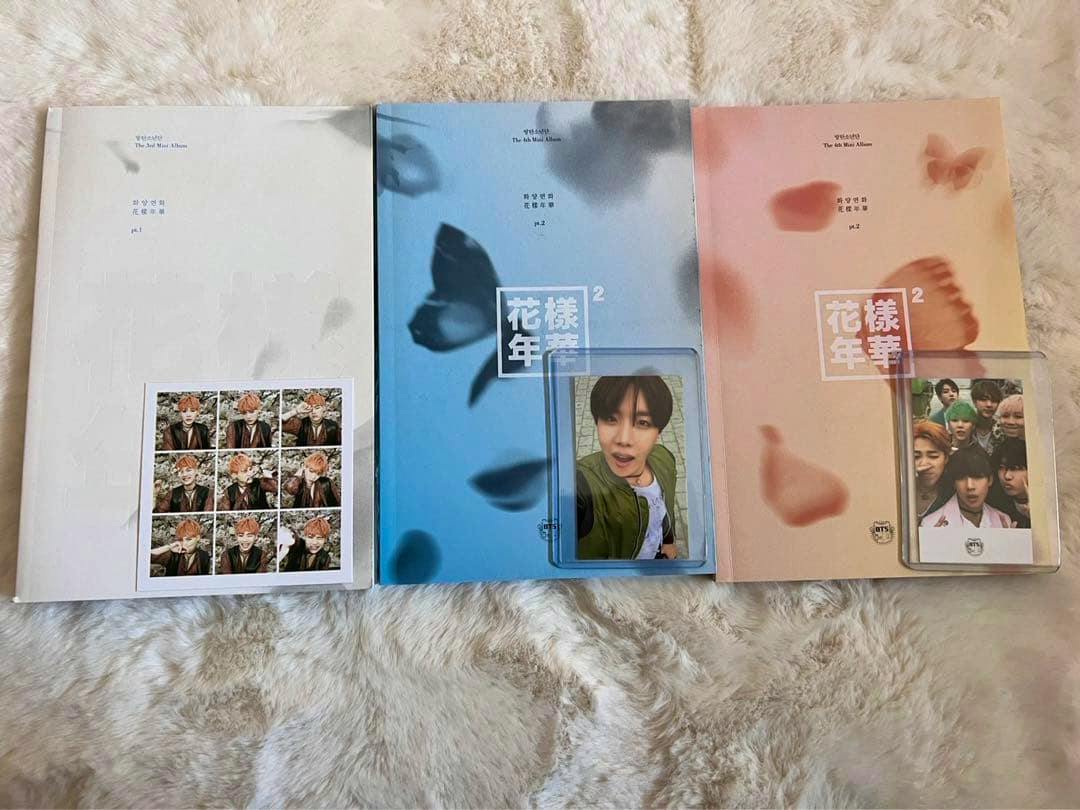Three copies of the BTS album “花様年華” displayed on a fur surface with two photocards placed on top.