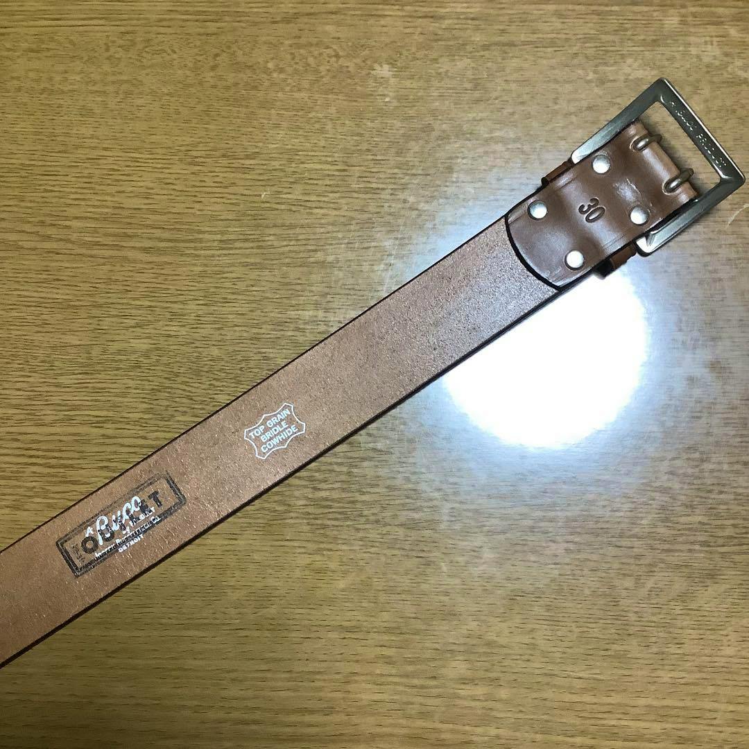 Brown BUCO leather belt laid flat on a wooden surface showing the metal buckle, rivets, and a "30" size stamp.