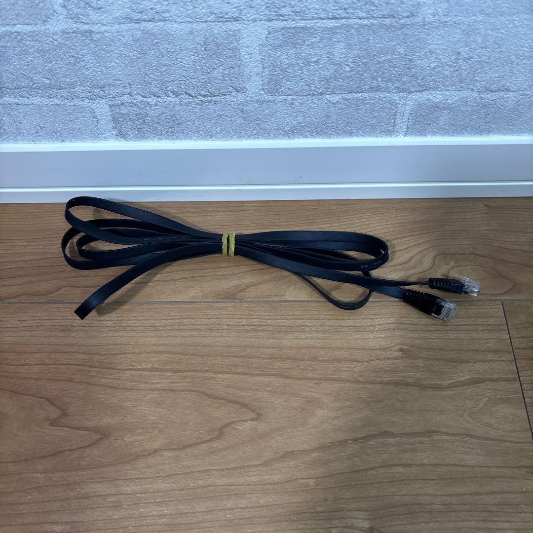 Black flat BUFFALO LAN cable (2m) with RJ45 connectors coiled on a wooden floor against a wall.