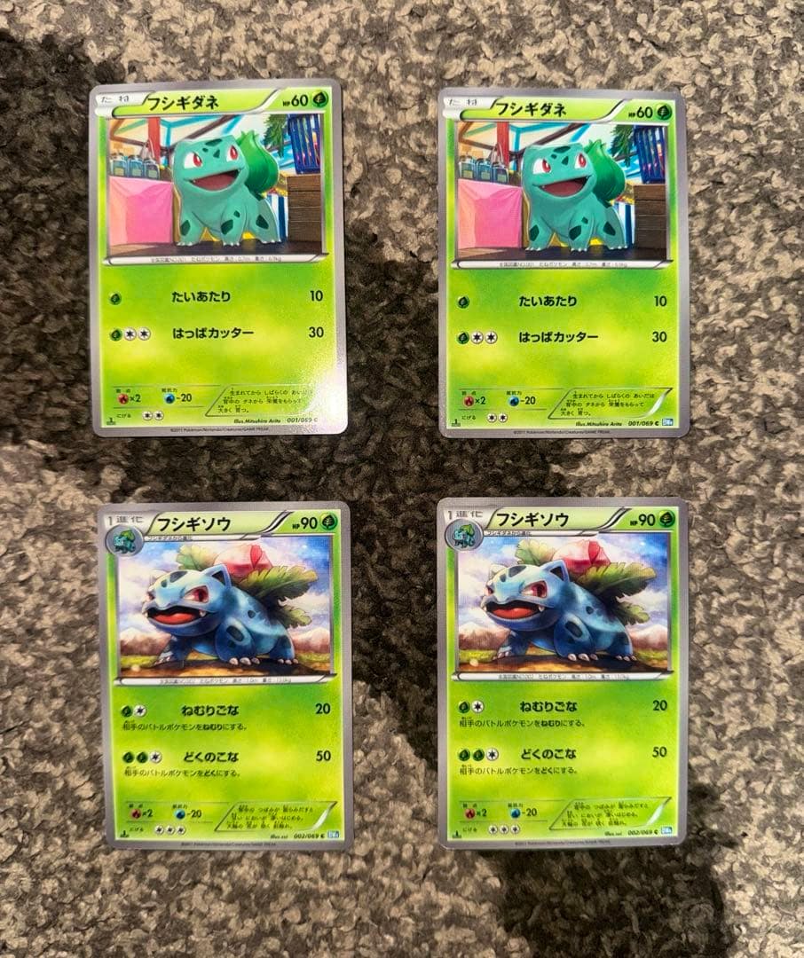 Four Pokémon trading cards (two フシギダネ and two フシギソウ) arranged in a 2x2 grid on a carpeted surface.