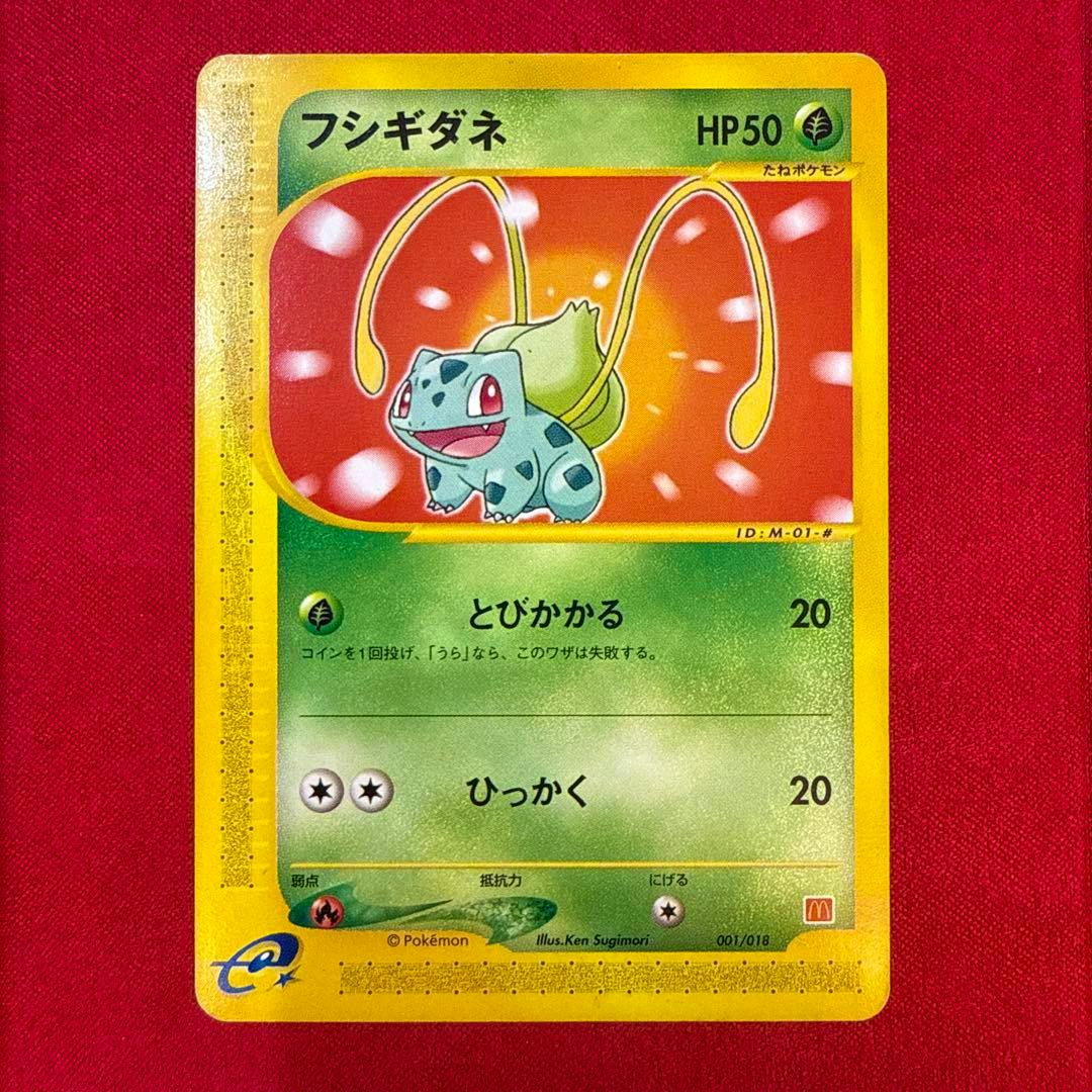 Front of the フシギダネ (Bulbasaur) Pokémon trading card showing the artwork, HP50, and attack text on a red background.