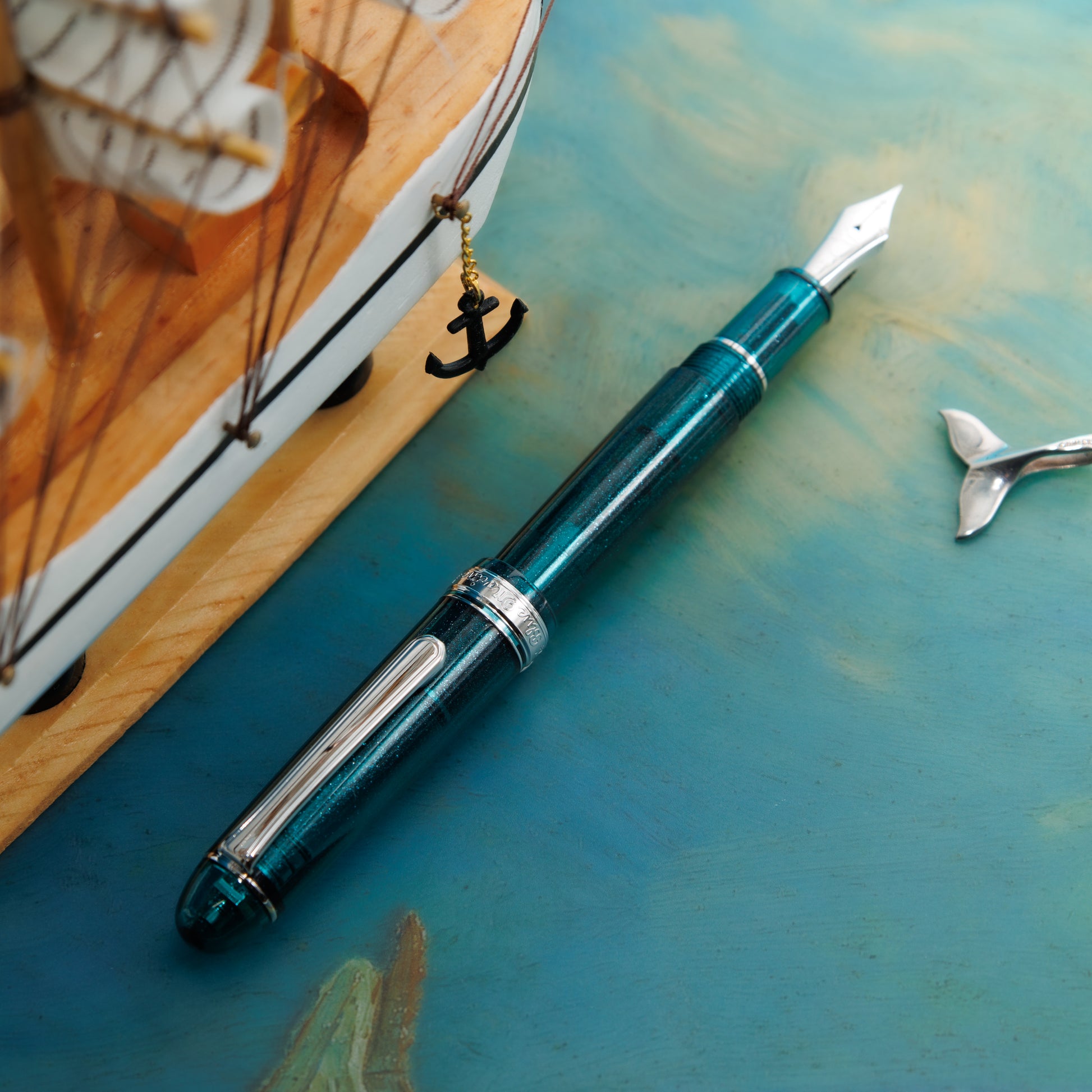 Blue Marine #3776 fountain pen shown uncapped on a teal surface beside a model ship.